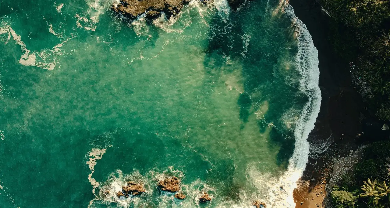 Aerial view of a turquoise cove and dark-sand beach on the Montezuma coast, Costa Rica